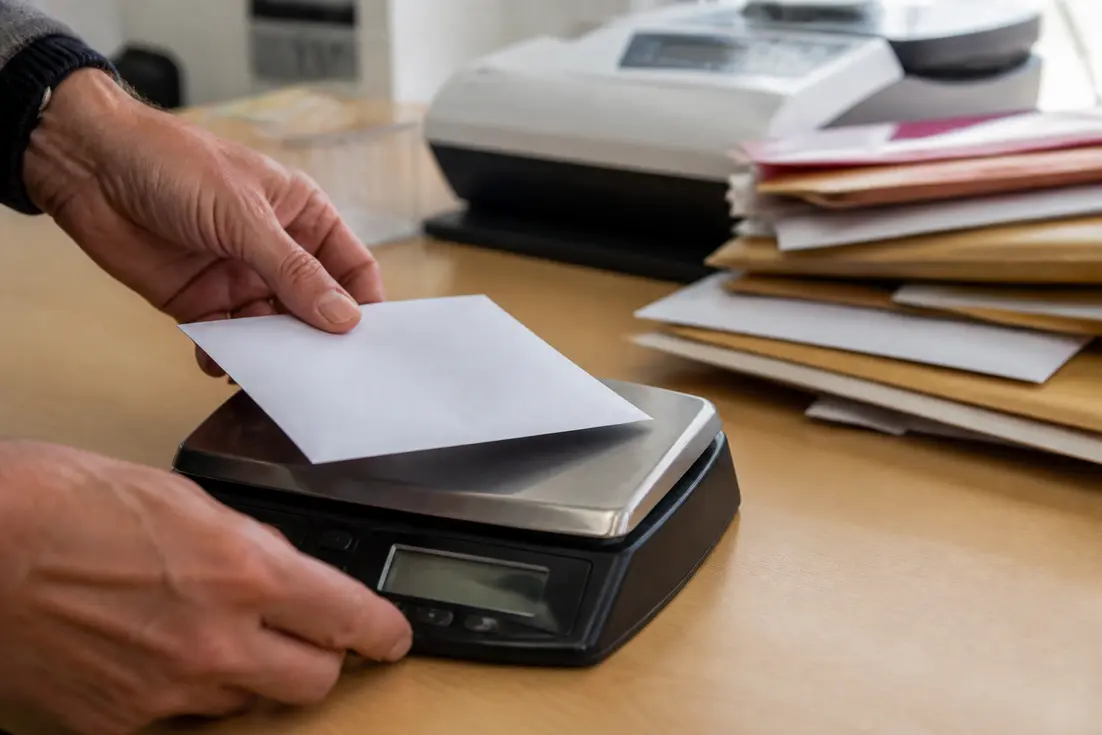 Main de personne ajustant une lettre sur une balance pour l'affranchissement avant envoi postal.