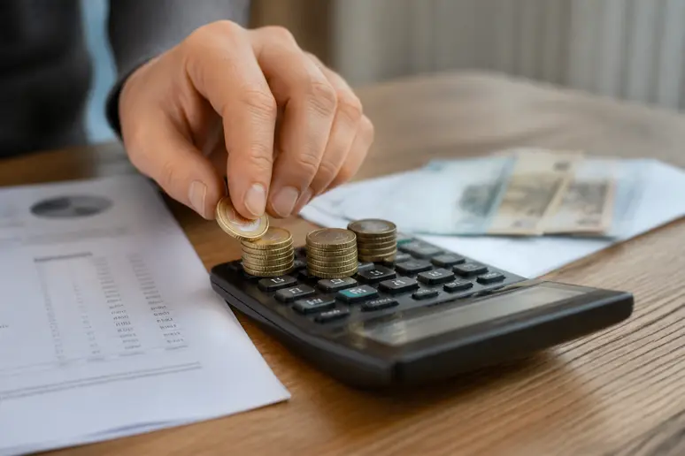 Main plaçant des pièces sur une calculatrice à côté de documents financiers.