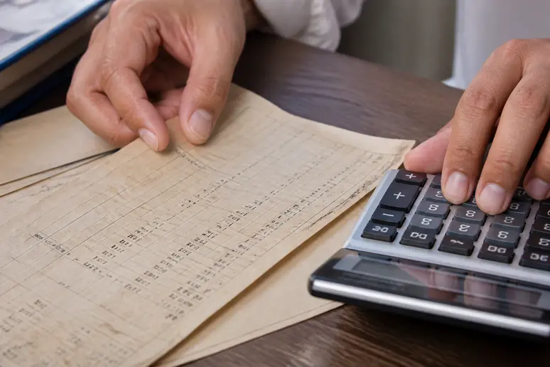 Mains tenant une calculatrice à côté d'un document affichant des chiffres.