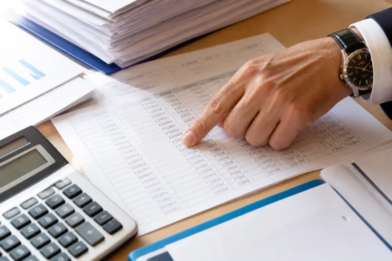Gros plan sur des documents financiers avec des chiffres et un doigt pointant un montant.