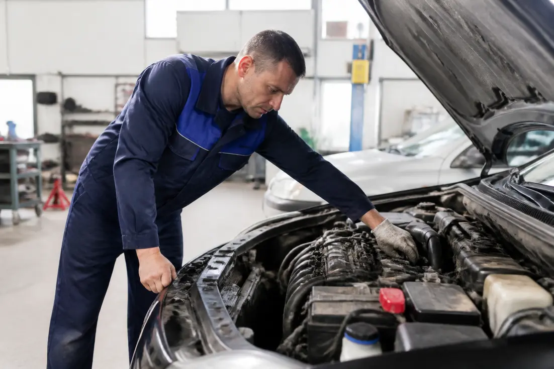 Un garagiste vérifie le moteur d'une voiture d'occasion dans un atelier, illustrant le malus voiture occasion.