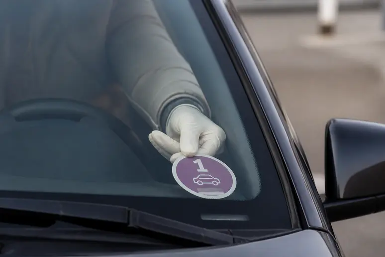 Main gantée collant une vignette Crit'Air sur le coin inférieur droit d'un pare-brise de voiture.