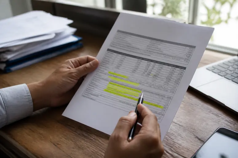 Mains posant une facture commerciale et un stylo sur un bureau en bois lors d'un rappel de paiement.